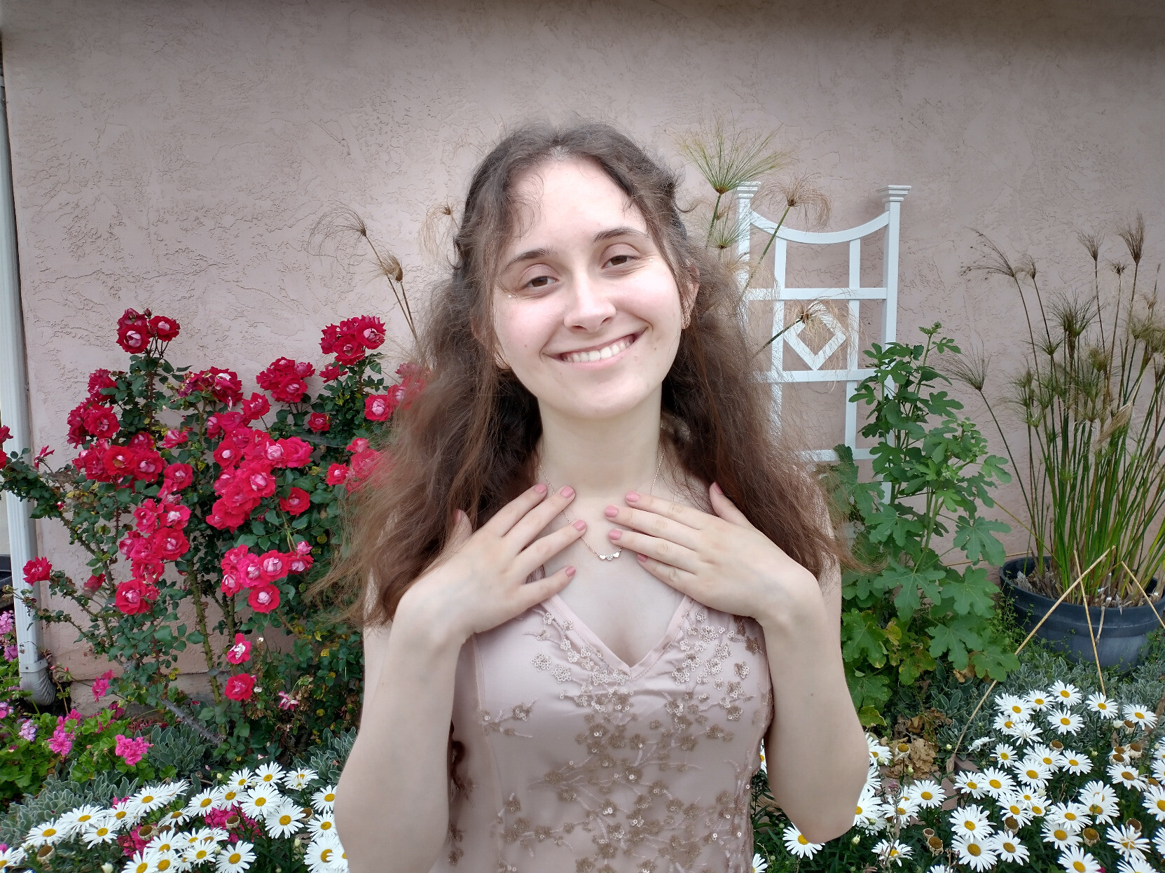 Closeup of a brunette girl (me!) wearing a rose pink dress. Her hands are on her chest and she is wearing a heart necklace.